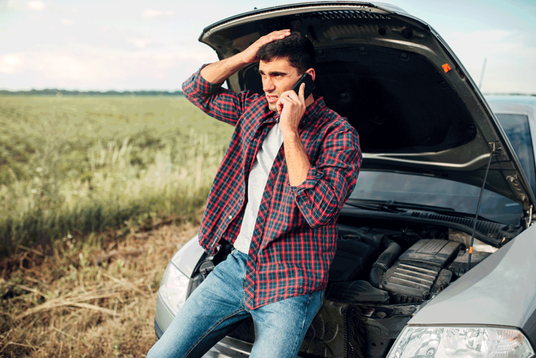 Man sitting on broken down car and calling a mechanic