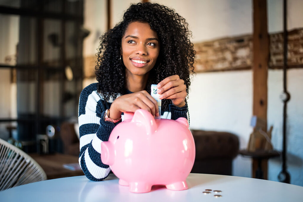 Young lady putting her savings into a piggy bank.