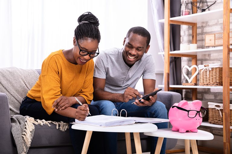 Young Couple Sitting On Sofa Calculating Savings